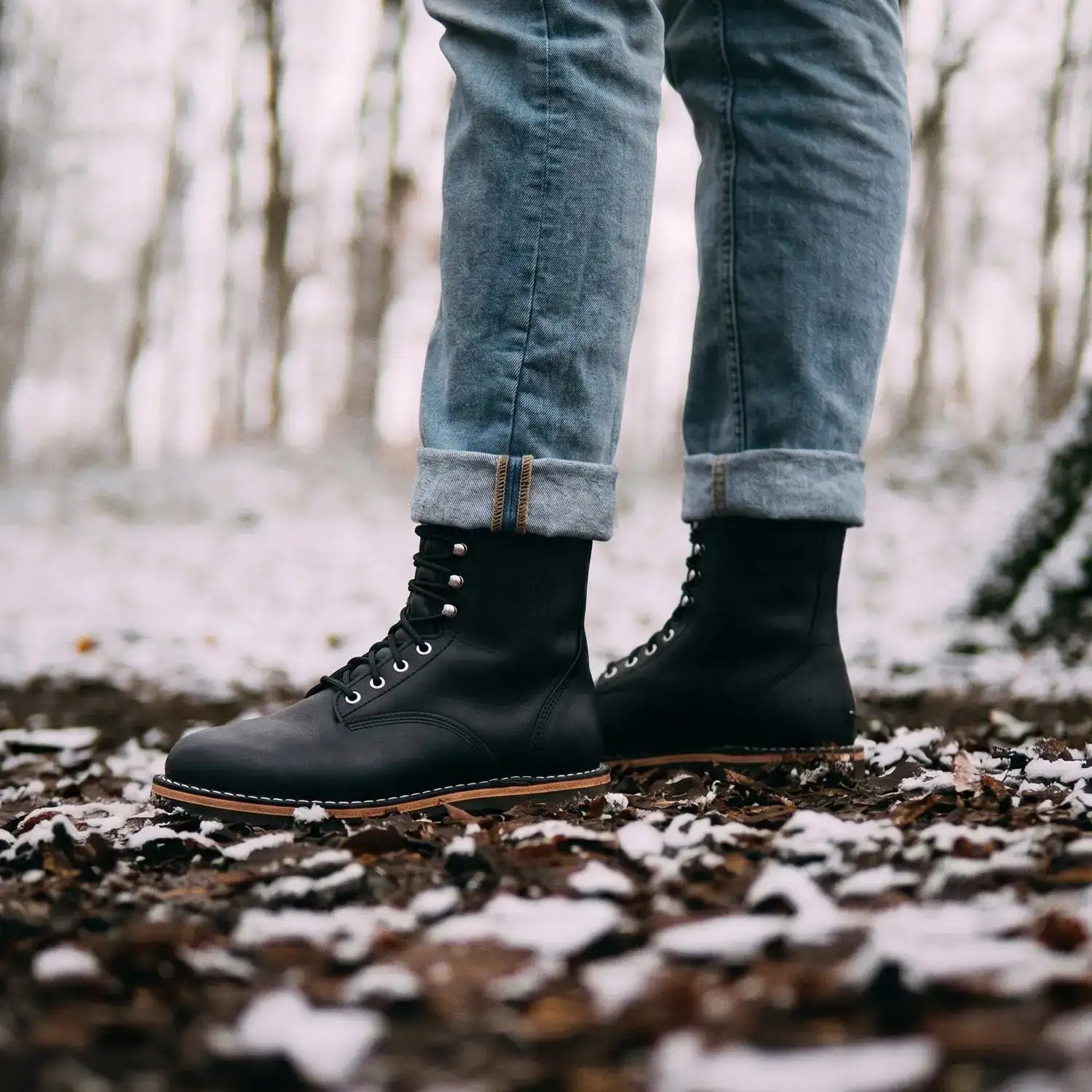 Black leather lace-up work boots with tan soles and silver eyelets.