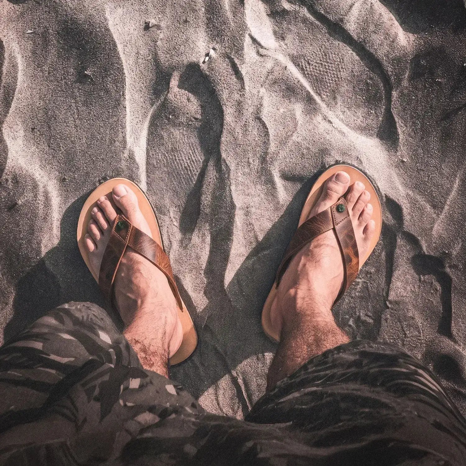 Brown leather flip-flops with a green gemstone accent on the strap.